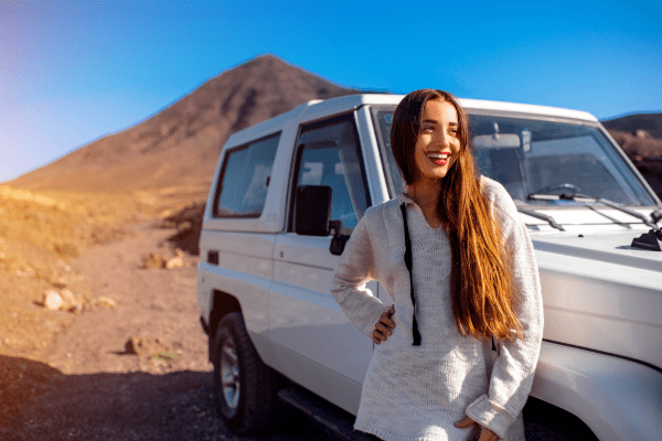 Smiling traveler standing next to a 4x4 vehicle in the desert of Egypt with mountains in the background.