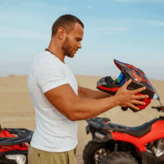 Man holding a motorcycle helmet outdoors. Morning Quad Bike Desert Safari
