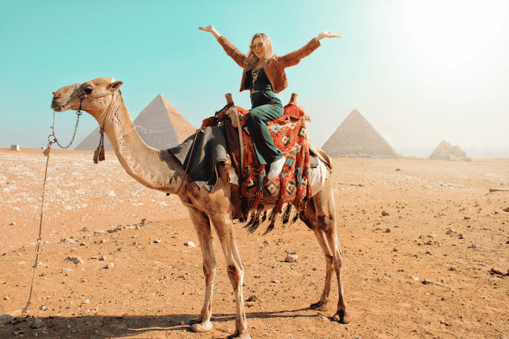 Person riding camel near pyramids in desert