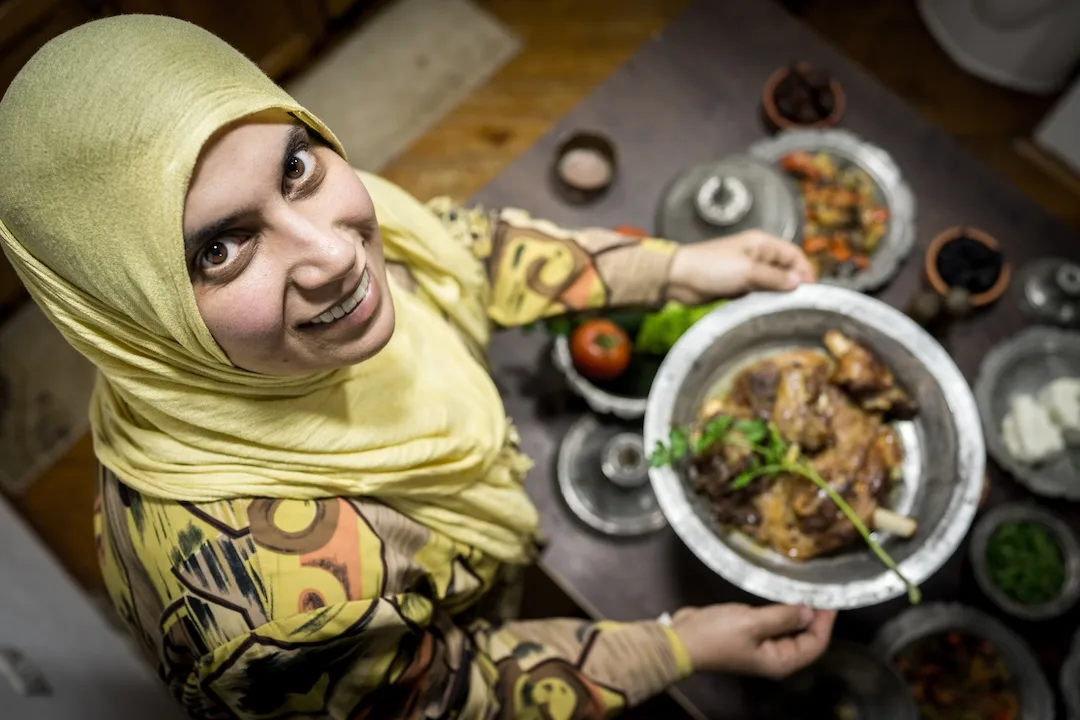 Woman presenting traditional dish, smiling in kitchen.