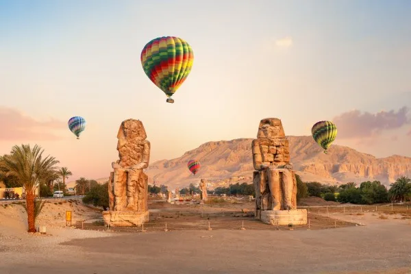 Hot air balloons over ancient Egyptian statues at sunrise.