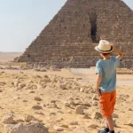 Child observing the Great Pyramid of Giza in Egypt while standing on the sandy desert.