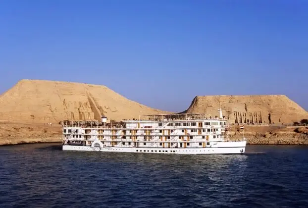 White cruise ship sailing by desert cliffs