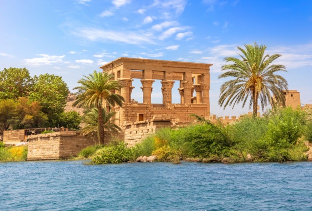 Temple near a river, surrounded by palm trees.
