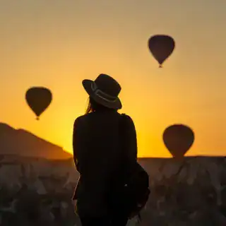 Rear view of silhouette young woman looking at hot air balloons while standing on land at Goreme, Ca