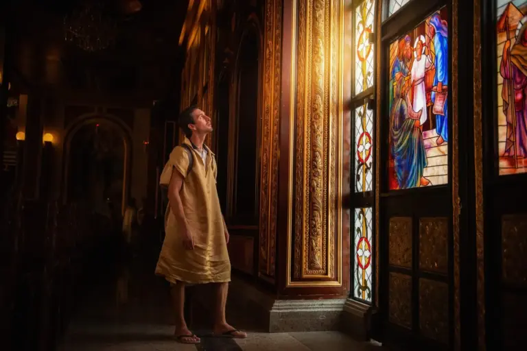 young man tourist stands at painted window in Coptic church in Egypt, looking at the falling light