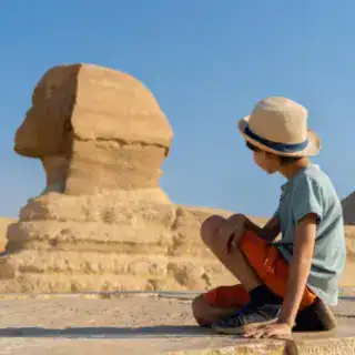 a boy sitting on a stone ledge with Great Sphinx of Giza in the background on a Hurghada to Cairo by bus excursion