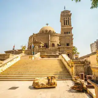 Exterior view of the historic St. George's Church in Cairo, showcasing its iconic tower and grand entrance stairs. Coptic Monasteries of St. Anthony & St. Paul