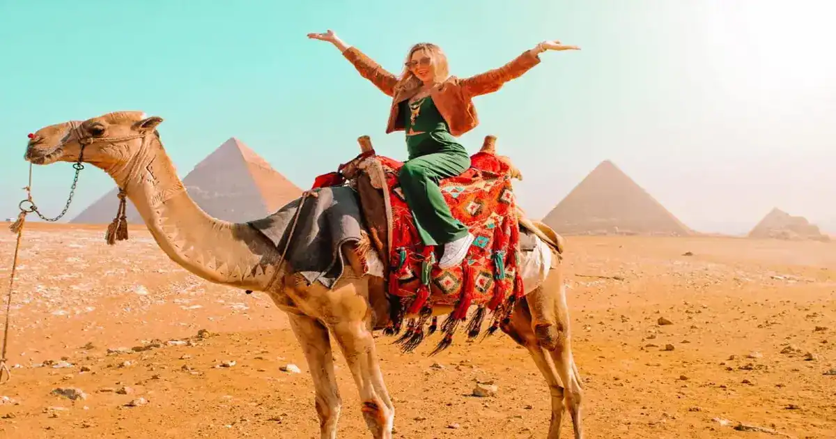 A traveler enjoying camel riding in front of the Great Pyramids of Giza.